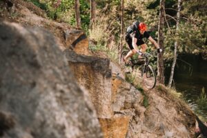 young trial biker riding downhill outdoors in pine forest